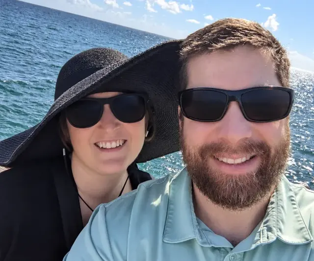 A smiling couple in sunglasses taking a selfie by the sea