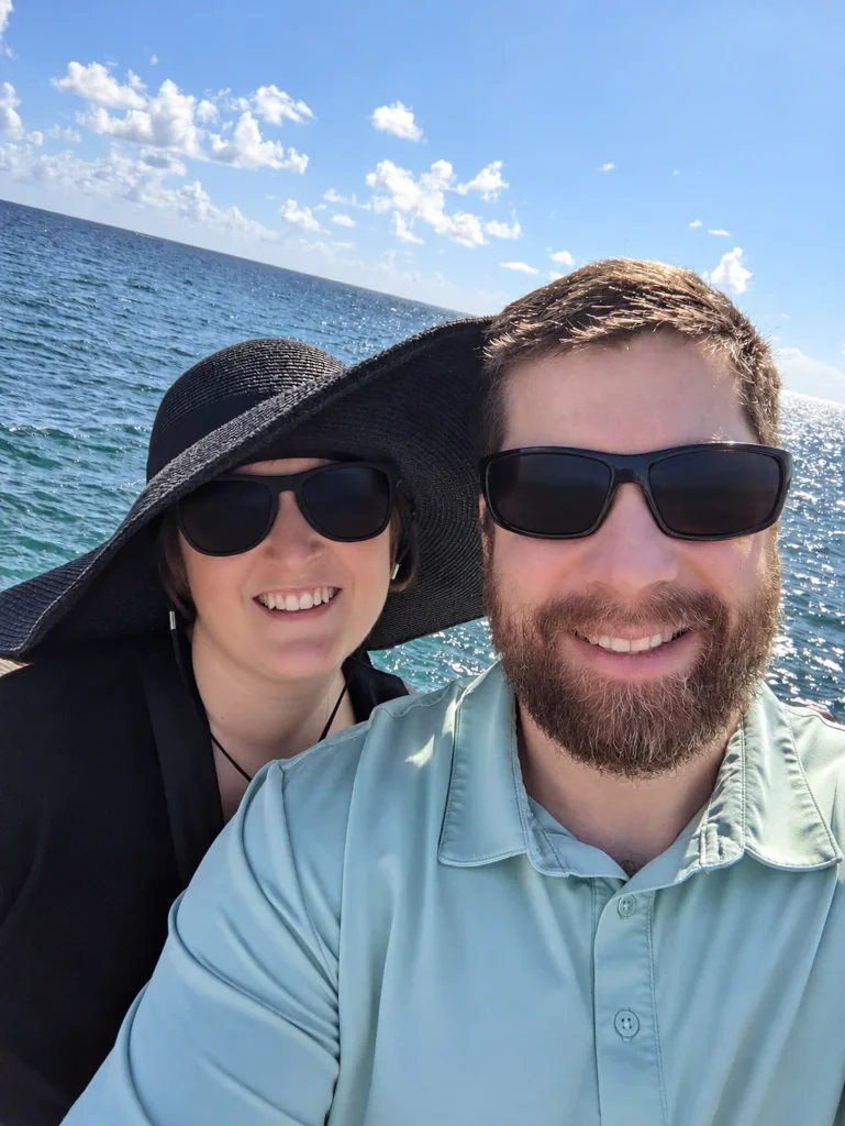 A smiling couple in sunglasses taking a selfie by the sea
