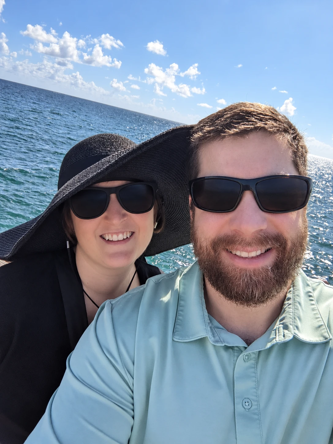 A smiling couple in sunglasses taking a selfie by the sea